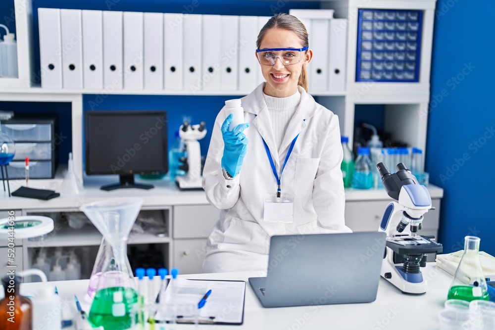 Young woman scientist smiling confident holding pills at laboratory Young woman scientist smiling confident holding pills at laboratory
