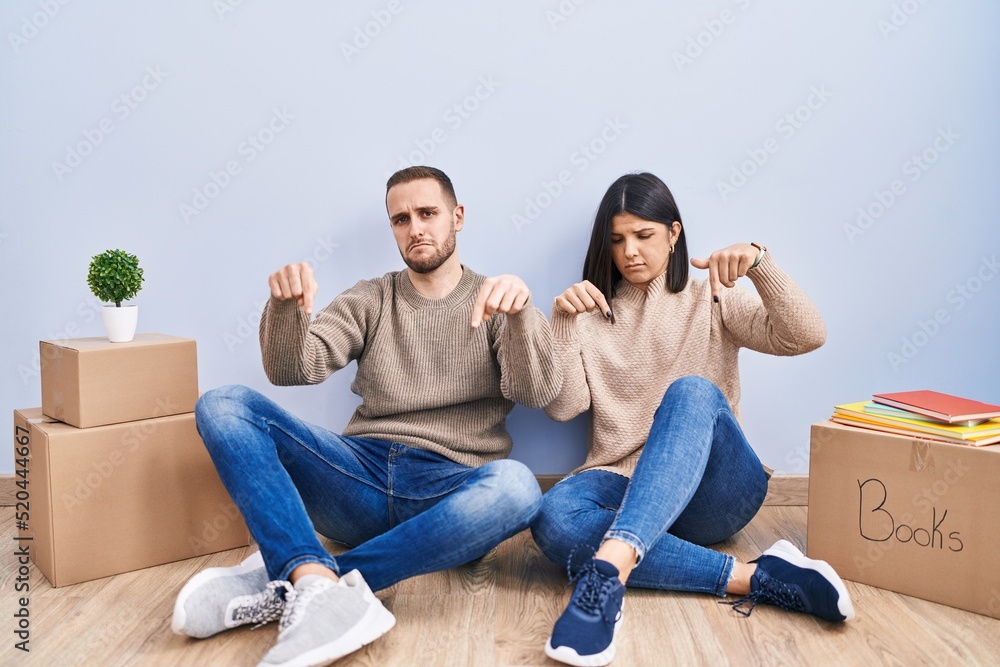 Young couple moving to a new home pointing down looking sad and upset, indicating direction with fingers, unhappy and depressed. Young couple moving to a new home pointing down looking sad and upset, indicating direction with fingers, unhappy and depressed.