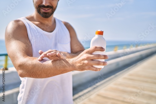 Hispanic sports man wearing workout style applying sunscreen on arm outdoors on a sunny day