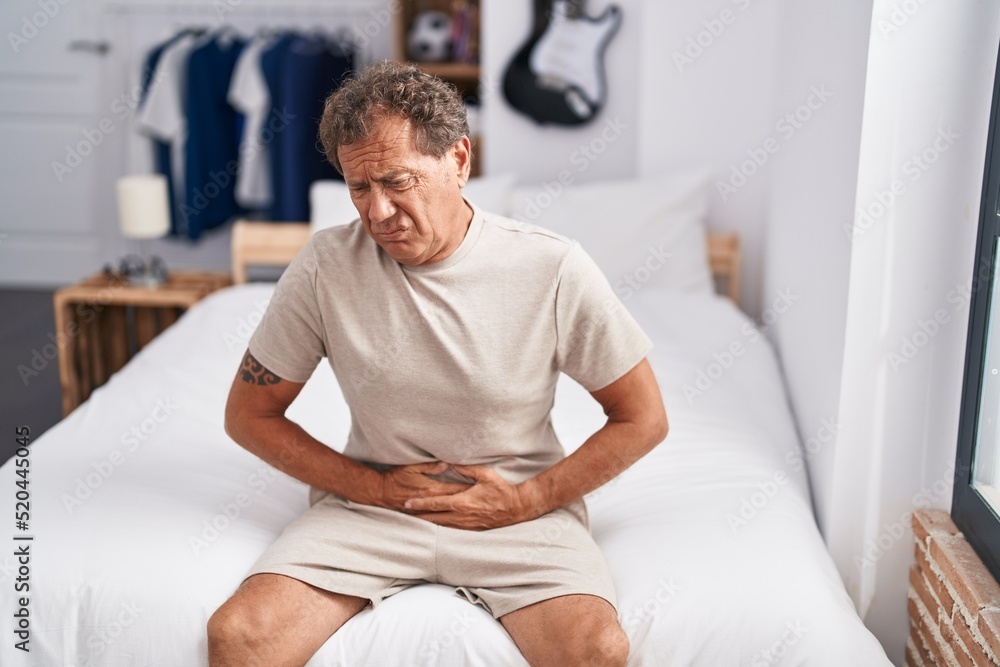 Middle age man suffering for stomachache sitting on bed at bedroom