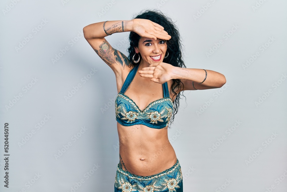 Fototapeta premium Young woman wearing bindi and traditional belly dance clothes smiling cheerful playing peek a boo with hands showing face. surprised and exited