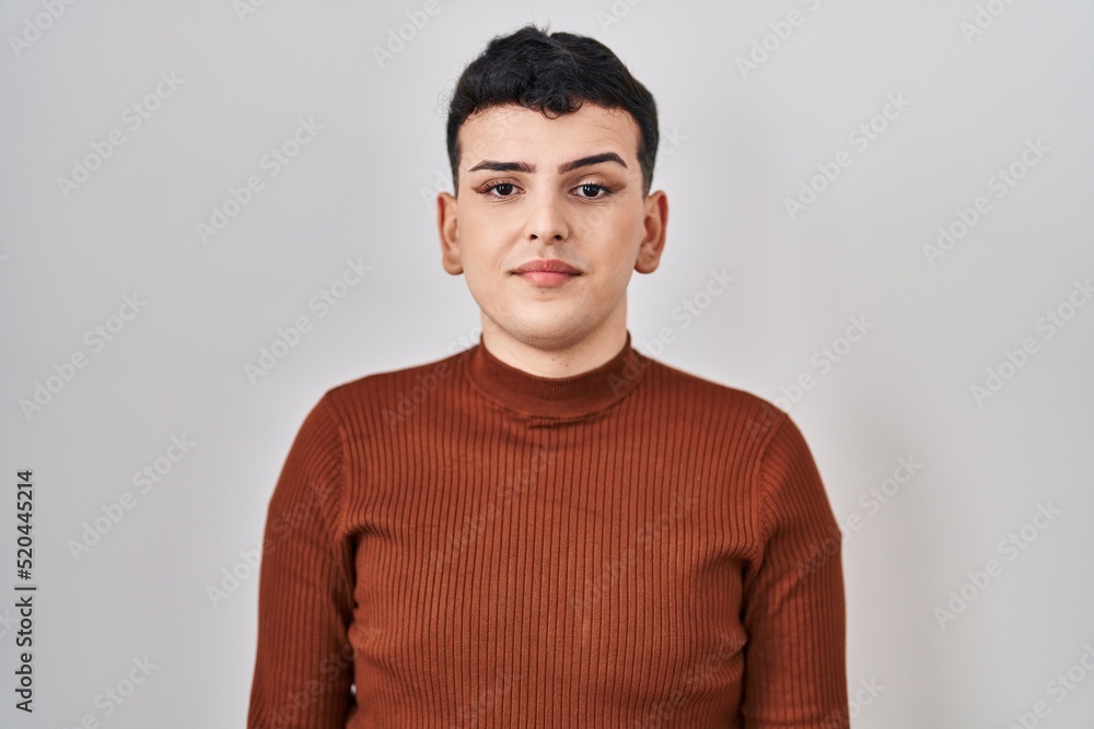 Non binary person wearing make up standing over isolated background with serious expression on face. simple and natural looking at the camera. Non binary person wearing make up standing over isolated background with serious expression on face. simple and natural looking at the camera.