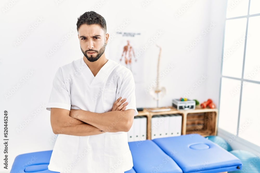 Obraz premium Young handsome man with beard working at pain recovery clinic skeptic and nervous, disapproving expression on face with crossed arms. negative person.
