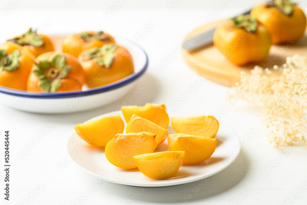Sliced ripe persimmon fruit on plate with white background