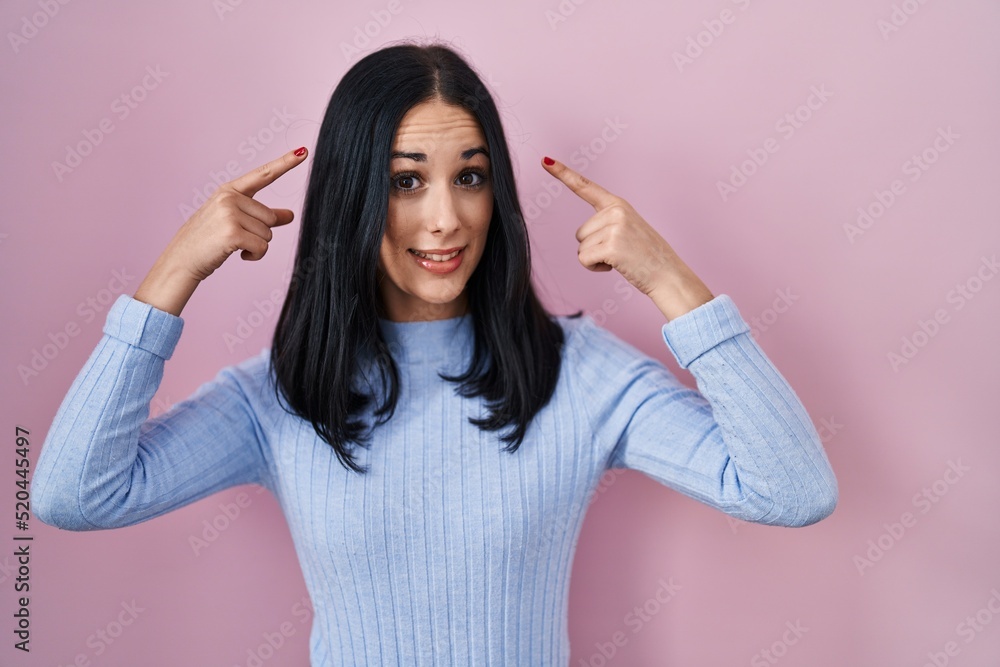 Hispanic woman standing over pink background smiling pointing to head with both hands finger, great idea or thought, good memory Hispanic woman standing over pink background smiling pointing to head with both hands finger, great idea or thought, good memory