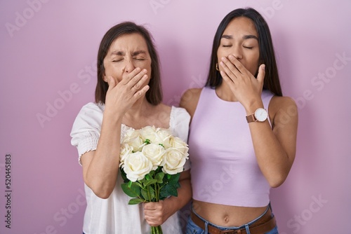 Hispanic mother and daughter holding bouquet of white flowers bored yawning tired covering mouth with hand. restless and sleepiness.