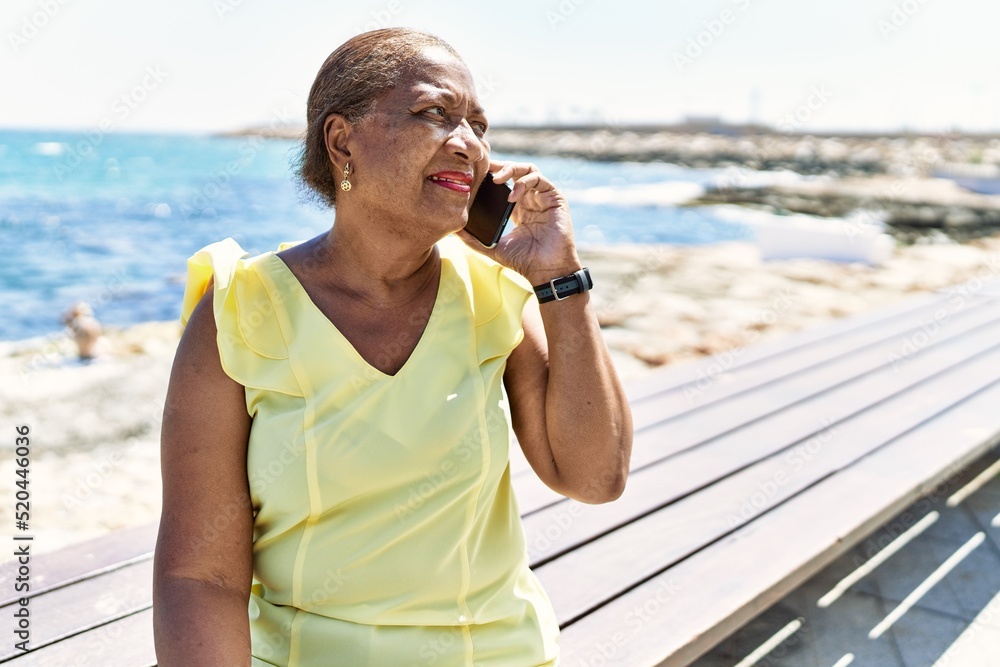 Senior african american woman talking on the smartphone sitting on the bench at the beach.