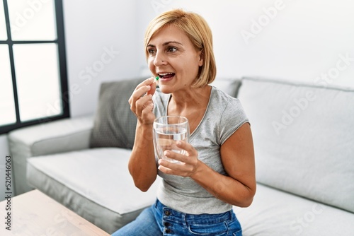 Middle age blonde woman smiling confident taking pill at home