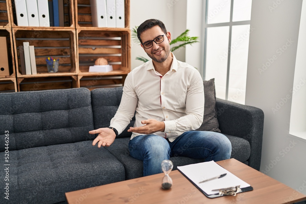 Young hispanic man with beard working at consultation office inviting to enter smiling natural with open hand Young hispanic man with beard working at consultation office inviting to enter smiling natural with open hand