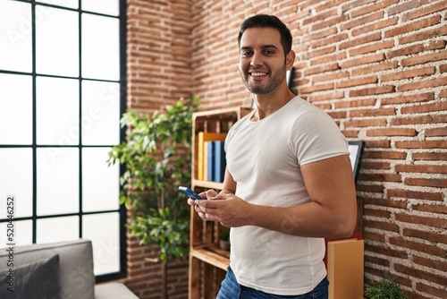 Young hispanic man smiling confident using smartphone at home photo