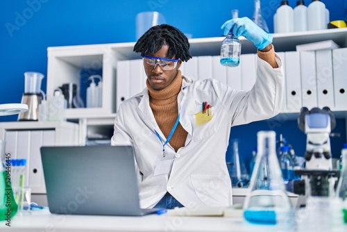 Fototapeta Naklejka Na Ścianę i Meble -  African american man scientist using laptop measuring liquid at laboratory