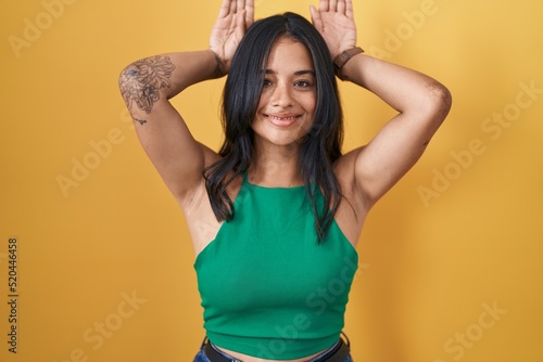 Brunette woman standing over yellow background doing bunny ears gesture with hands palms looking cynical and skeptical. easter rabbit concept. photo