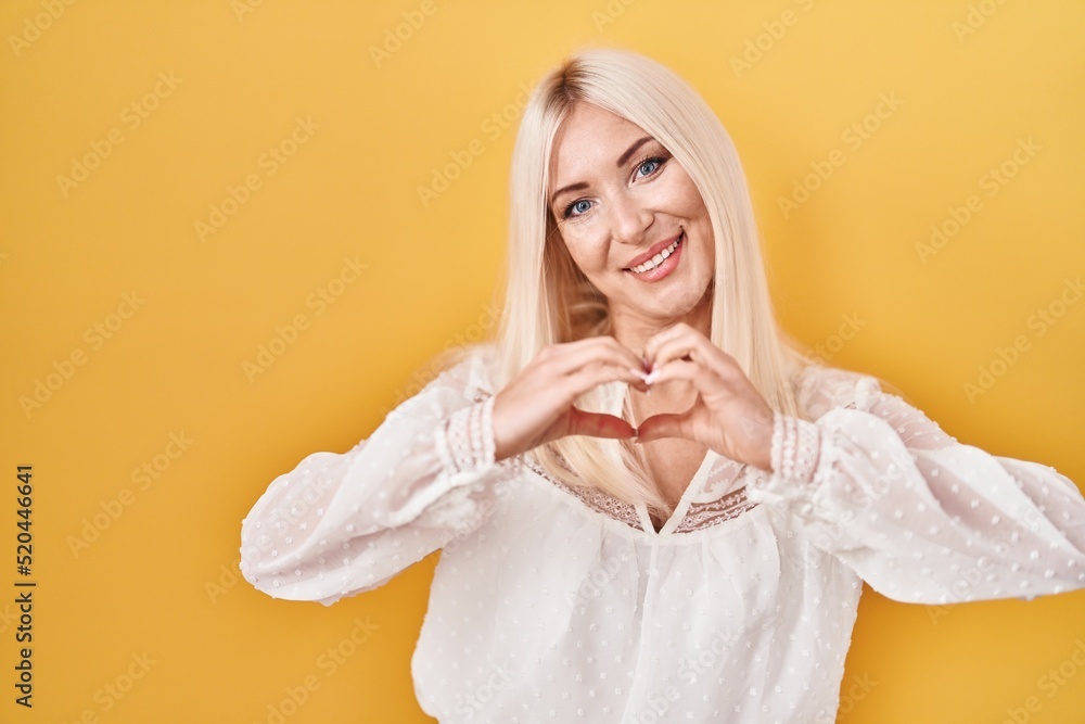 Caucasian woman standing over yellow background smiling in love showing heart symbol and shape with hands. romantic concept. Caucasian woman standing over yellow background smiling in love showing heart symbol and shape with hands. romantic concept.
