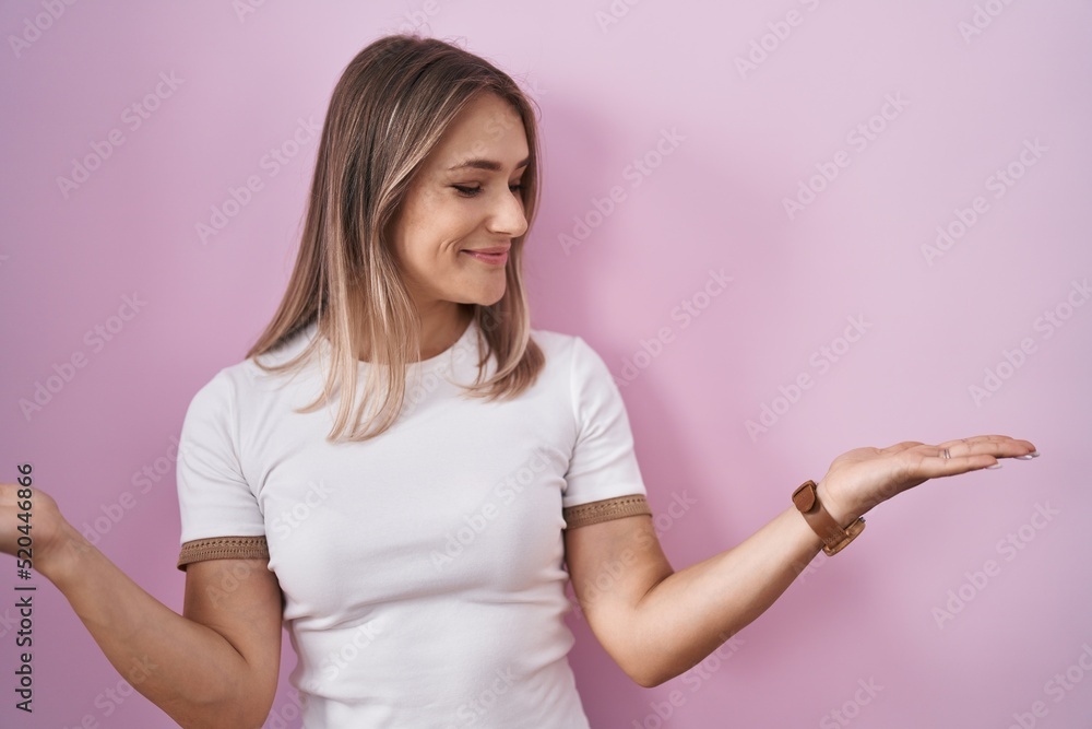 Blonde caucasian woman standing over pink background smiling showing both hands open palms, presenting and advertising comparison and balance Blonde caucasian woman standing over pink background smiling showing both hands open palms, presenting and advertising comparison and balance
