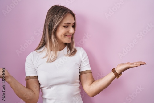 Blonde caucasian woman standing over pink background smiling showing both hands open palms, presenting and advertising comparison and balance © Krakenimages.com