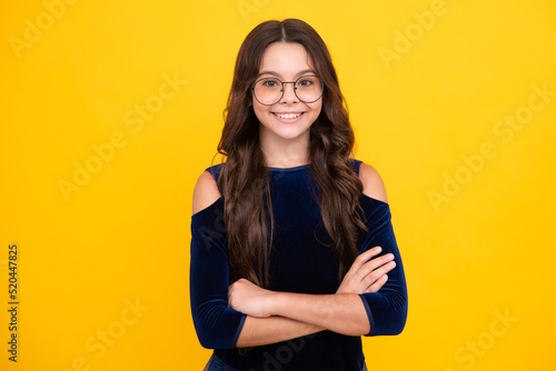Happy face, positive and smiling emotions of teenager girl. Confident child keep arms crossed, isolated on yellow background, empty space. Little caucasian teenage girl 12, 13, 14 years old hold hands