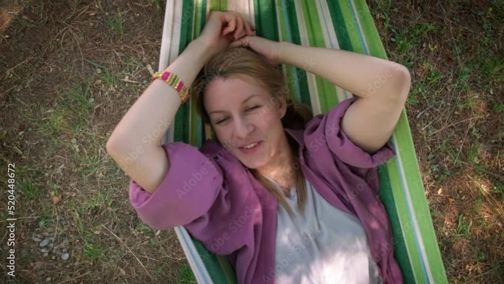 Happy young woman lying and swinging in hammock and smiling, top down shot.