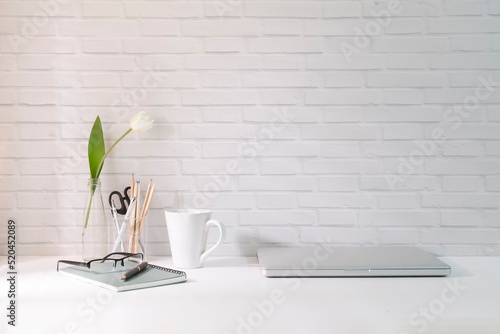 Minimal workplace with laptop, coffee cup and stationery on white table.