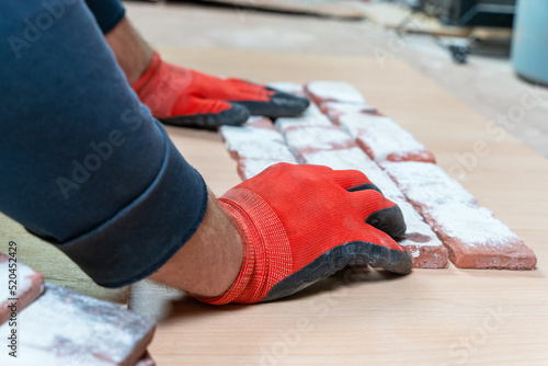 Hands of craftsman in red gloves on carpenter table in workshop over decorative brick close-up. Process of making decorative bricks imitating antiquity based on ancient casts. Decorative gypsum tiles