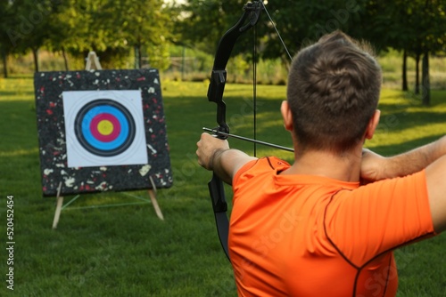 Fotografiet Man with bow and arrow aiming at archery target in park, back view