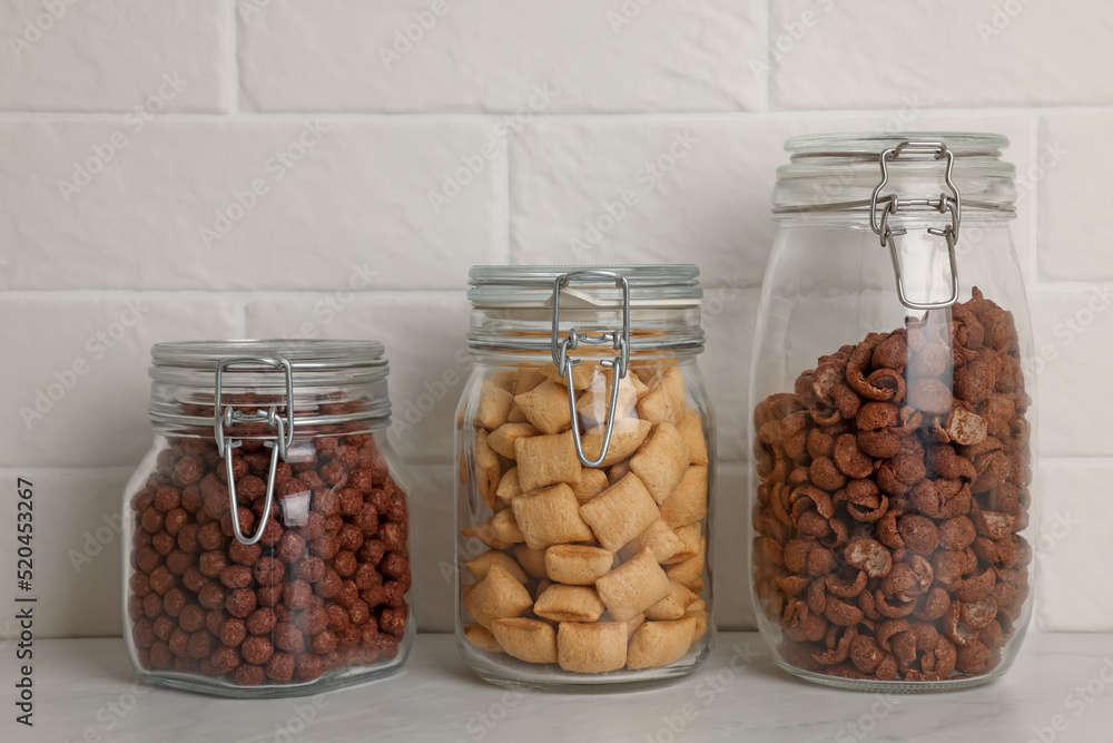 Glass containers with different breakfast cereals on white countertop near brick wall Glass containers with different breakfast cereals on white countertop near brick wall