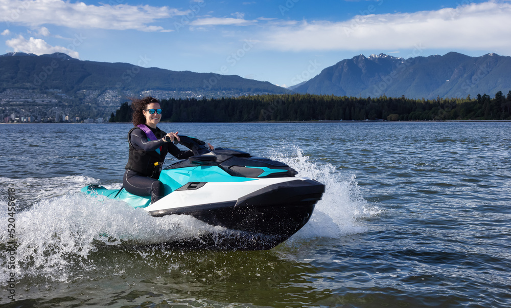 Adventurous Caucasian Woman on Jet Ski riding in the Ocean. Modern City in background. Downtown Vancouver, British Columbia, Canada.