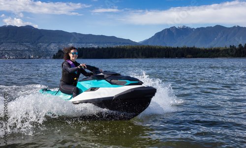 Adventurous Caucasian Woman on Jet Ski riding in the Ocean. Modern City in background. Downtown Vancouver, British Columbia, Canada.
