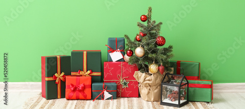 Heap of Christmas gift boxes with fir tree near green wall in room