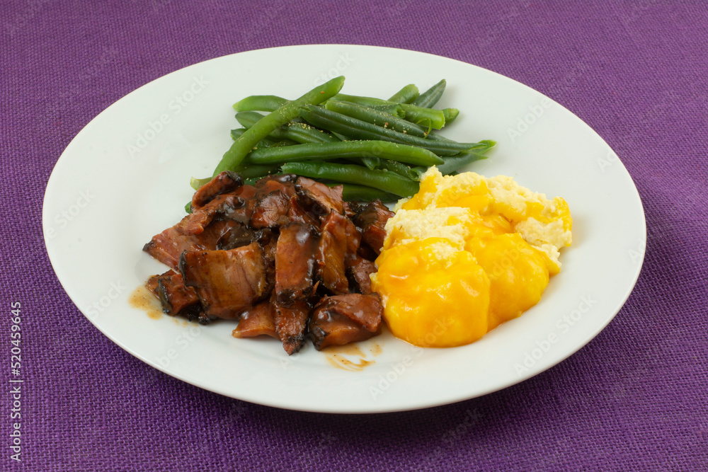 Warm freshly cooked dinner of beef brisket with barbecue sauce and seasoned green beans and grits with cheese on plate