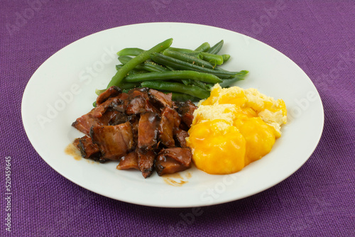 Warm freshly cooked dinner of beef brisket with barbecue sauce and seasoned green beans and grits with cheese on plate