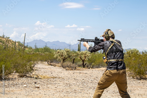 Military special forces person shooting ar15 pistol gun while wearing ear protection and looking through holosight of custom weapon photo