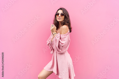 Young beautiful smiling cute romantic woman in trendy summer dress. Carefree woman posing in the street near pink wall. Positive model outdoors in sunglasses. Cheerful and happy.