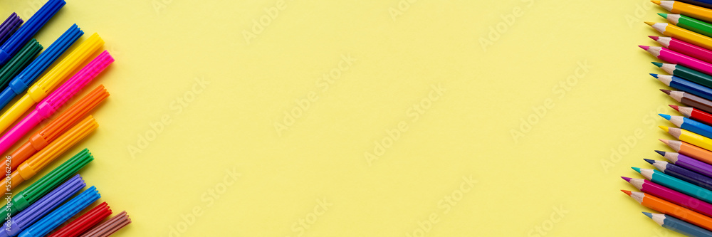 Colored wooden pencils row on one side and set of color felt pen or markers on second side. Close-up on yellow background with copy space. Banner, top view.