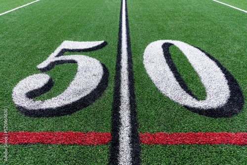 Synthetic turf football 50 yard line in white with black number shadow along with red lacrosse line and yellow soccer mid field line	