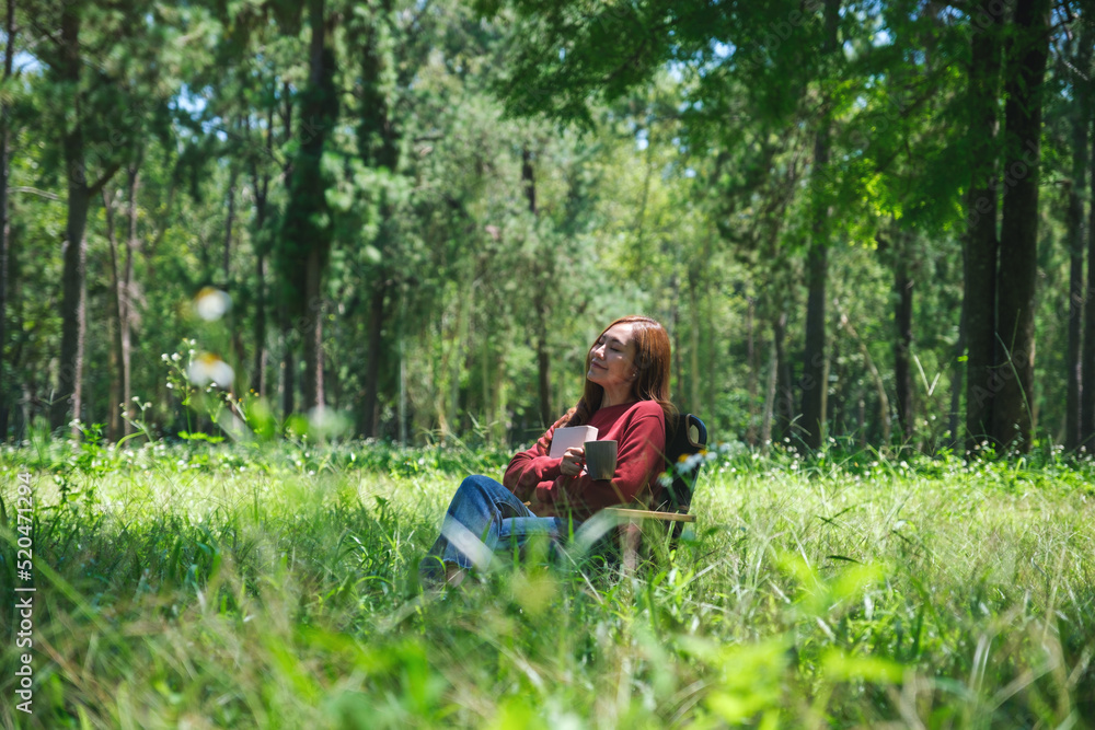 Portrait image of a beautiful young asian woman holding a book and coffee cup while sitting on a chair in the park Portrait image of a beautiful young asian woman holding a book and coffee cup while sitting on a chair in the park