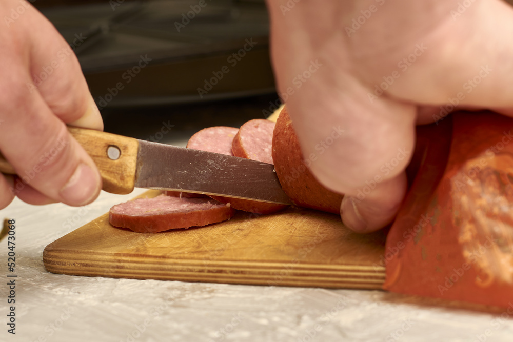 a man prepares sandwiches in a sandwich maker cuts sausage with a knife on a wooden cutting board a man prepares sandwiches in a sandwich maker cuts sausage with a knife on a wooden cutting board