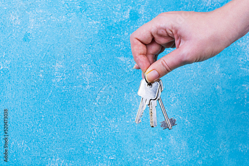 Female hand holding keys on blue background