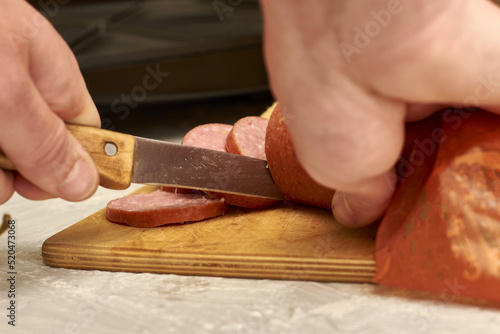 a man prepares sandwiches in a sandwich maker cuts sausage with a knife on a wooden cutting board