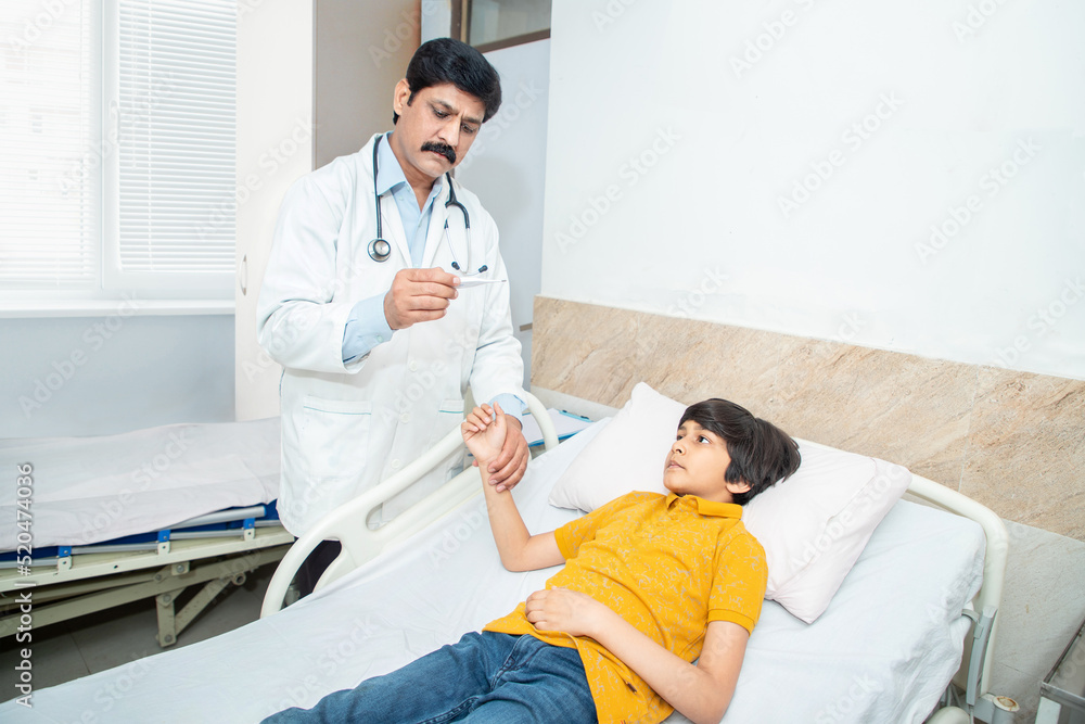 Indian doctor check fever of boy kid using thermometer, sick child lying at hospital bed. Indian doctor check fever of boy kid using thermometer, sick child lying at hospital bed.
