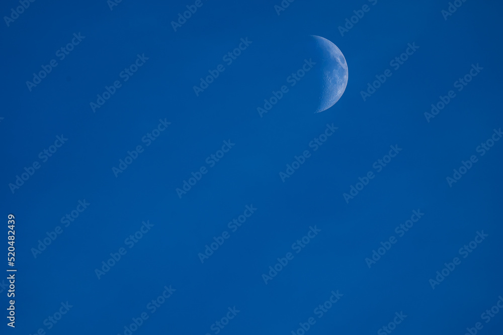 the growing moon in the first quarter with craters on the background of the blue evening sky the growing moon in the first quarter with craters on the background of the blue evening sky
