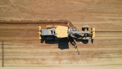 Road construction grader aerial view. The grader levels the sand for further road construction. Road construction works. Heavy machinery. Aerial footage.