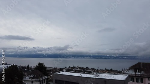 Moving timelapse; cloudy day over the geneva lake during the winter, snowy french mountains behind