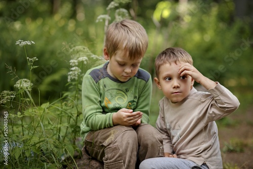 little cute boys examining a snail. One boy is sitting on rock and holding a snail in hands  another boy is sitting on his haunches and looking back.