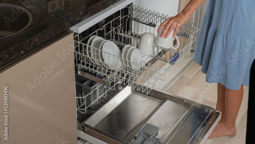 A woman takes clean dishes out of the dishwasher