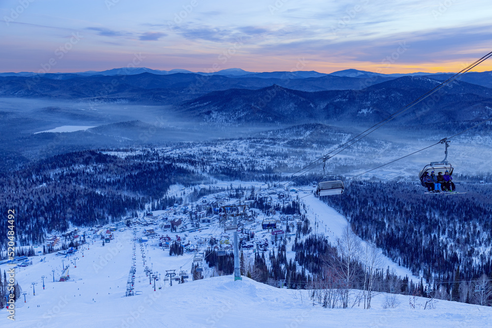 View from mount peak on Sheregesh ski resort and Altai mountains or Gornaya Shoria. Active winter rest, skiers and snowboarders on ski slope and Ski lift, morning and sunrise, sunlight.