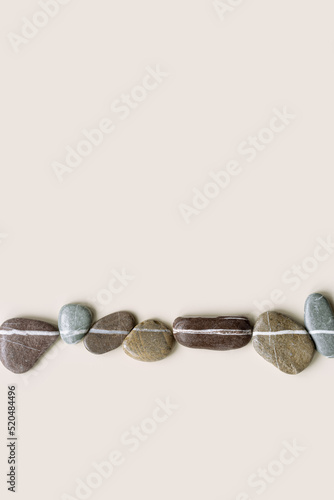 Creative arrangement of natural colored stones. Smooth pebbles in row on beige background. Minimal trend summer flat lay, top view still life composition with sea pebble on the same line
