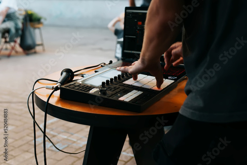 Side view of unrecognizable street musician beatmaker playing hip hop beats on drum machine midi controller at open air festival, selective focus