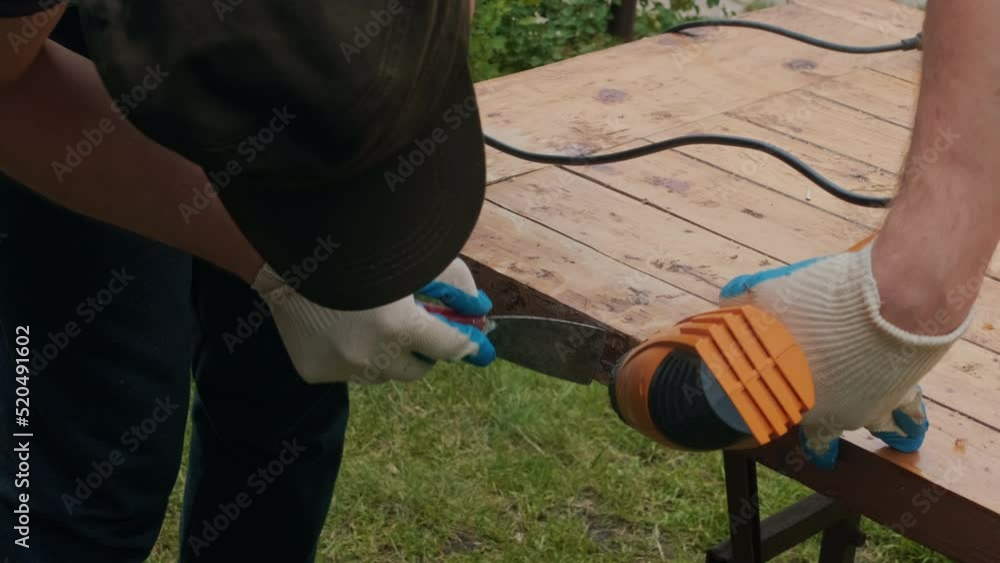 Man removing old varnish and paint from wood using scraper and heat gun. Restoration work of old wooden table outdoors. Furniture repair, reuse of old things concept. Man removing old varnish and paint from wood using scraper and heat gun. Restoration work of old wooden table outdoors. Furniture repair, reuse of old things concept.