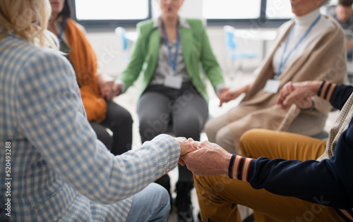 Group of senior people sitting in circle during therapy session, holding hands and praying together.