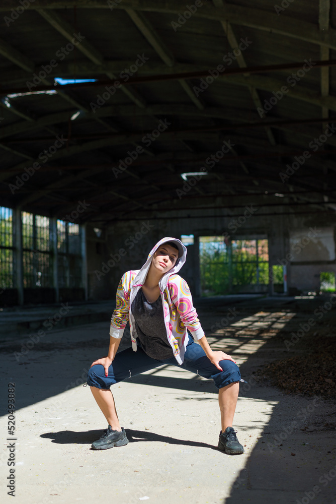 Young woman street dancer dancing and jumping in abandoned building on a sunny summer day